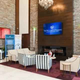 A modern hotel lobby featuring a seating area with elegant chairs, a chandelier, and a television on the wall.