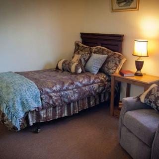 A cozy bedroom with a neatly made bed, a lamp on the nightstand, and an armchair beside it.