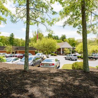 A serene view of a parking lot surrounded by trees, featuring a building in the background.