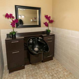 A well-equipped hair salon with a washing station featuring a sink, mirror, and decorative flowers.