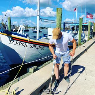 A person preparing for a fishing trip at the marina, with the boat 'Tarpon Springs' in the background.