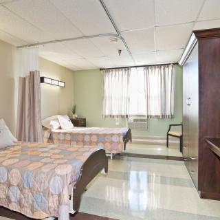 A hospital room with two beds, separated by a curtain, and a window providing natural light.