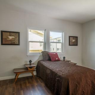 A cozy bedroom with a single bed, artwork on the walls, and natural light from two windows.