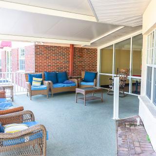A cozy outdoor patio space with rattan furniture and blue cushions under a covered roof.