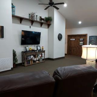 A cozy living room space featuring a television mounted on the wall, decorated shelves, and comfortable seating.