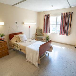 A well-lit hospital patient room featuring a bed, seating area, and window.