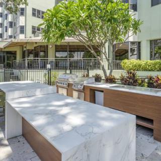 A modern outdoor barbecue area with marble countertops and lush greenery in an apartment complex.