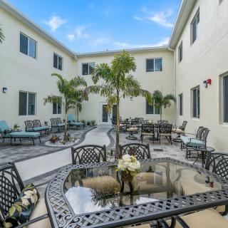 A courtyard with outdoor seating, featuring palm trees and surrounding building exterior.