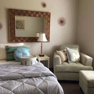 A cozy bedroom setup featuring a bed with decorative pillows, an armchair, and a stylish mirror.