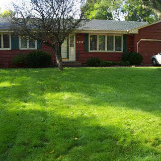 A suburban brick house with a well-maintained lawn and tree in front.