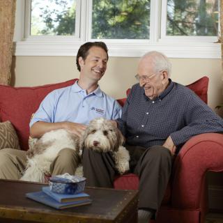 A happy moment shared between two men and a dog on a living room couch.