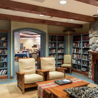 A cozy library room with bookshelves, armchairs, and a fireplace.