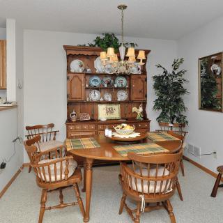 A cozy dining room with a wooden table, chairs, and a china cabinet displaying decorative plates.