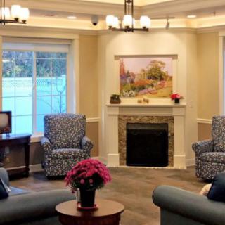 A cozy living room with comfortable seating arranged around a fireplace, featuring tasteful decor and a landscape painting above the mantel.