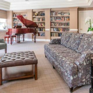 A cozy living room with a grand piano and bookshelves.