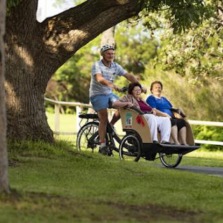 A caregiver enjoying a bike ride with two seniors in a park.