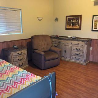A cozy bedroom with a patterned bedspread, an upholstered chair, and vintage-style furniture.