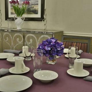 An elegantly set dining table with ceramic dishes and a purple floral centerpiece.