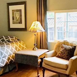 A cozy bedroom with a bed, armchair, side table, and lamp next to a window.