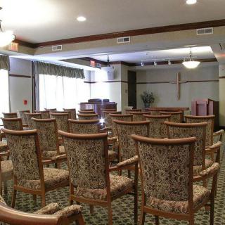 An indoor chapel with rows of chairs facing an altar and a cross on the wall.