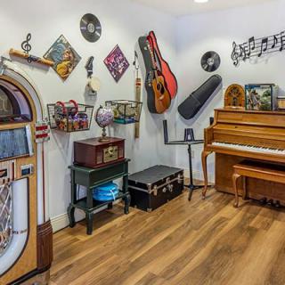 A cozy music room featuring a piano, jukebox, guitars, and musical-themed decorations.