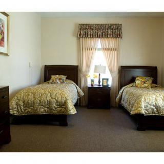A bedroom with two twin beds and matching bedding, featuring a nightstand between them and a window with curtains.