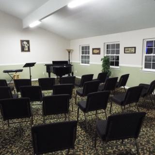 A small music room with rows of chairs facing a grand piano.