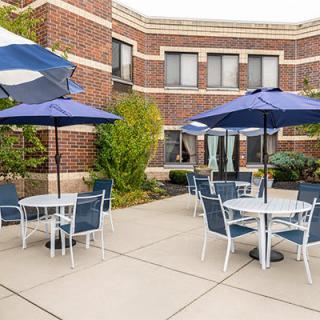 A well-maintained patio with tables, chairs, and umbrellas outside a brick building.