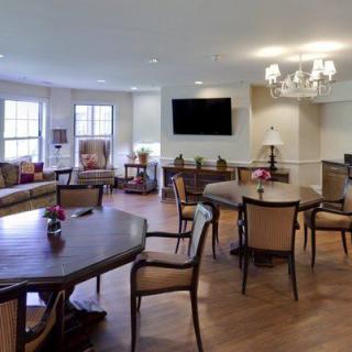 A spacious living room with elegant furniture, tables, chairs, and a flat-screen television.