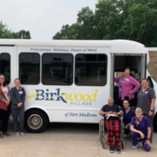 A group of people, possibly healthcare workers, posing in front of a bus labeled 'Birkwood'.