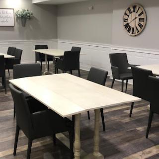 A modern dining area featuring simple tables and dark chairs, highlighted by a clock on the wall.