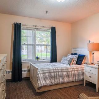 A cozy bedroom with a neatly made bed, dark curtains, and a bedside lamp.
