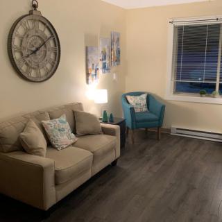 A cozy living room with a beige sofa, decorative clock, and a teal chair.