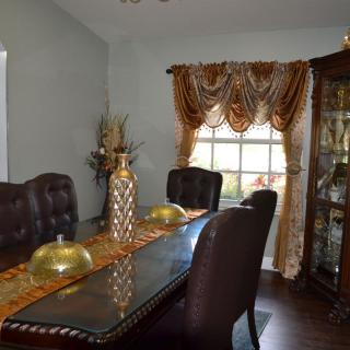 A well-decorated dining room with a glass table, elegant chairs, and luxurious curtains.
