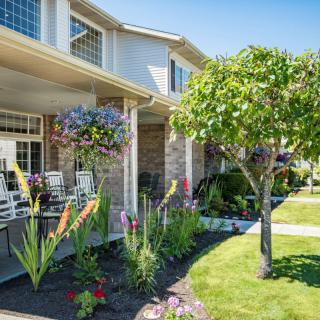 A beautiful suburban house with a well-maintained garden and porch under a clear blue sky.