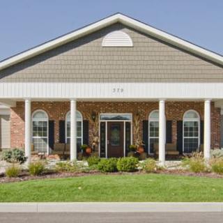 A suburban residential building with brick facade and white columns, surrounded by a landscaped front yard.
