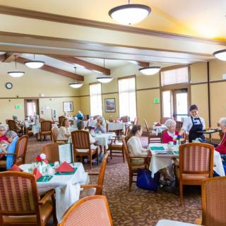 A dining area with seniors seated at tables, enjoying a meal in a well-lit room.