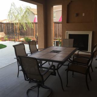 A cozy outdoor patio with a dining set and fireplace, overlooking a garden.