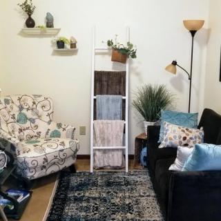 A cozy living room with a patterned armchair, dark sofa, decorative ladder, and floor lamp.