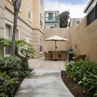A cozy courtyard with patio furniture and an umbrella, surrounded by plants and urban architecture.