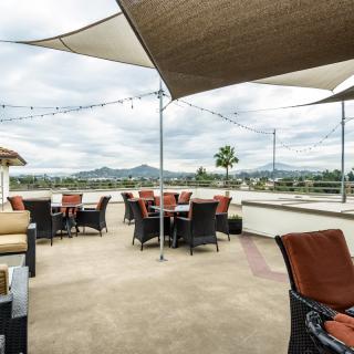 An outdoor patio with tables and chairs, shaded by sail canopies, offering a scenic mountain view.