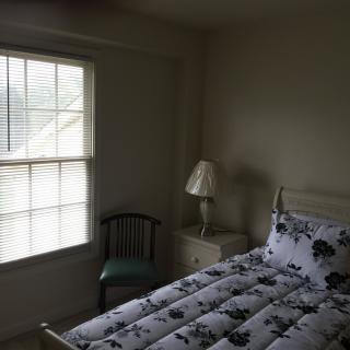 A cozy bedroom with a bed, a lamp on a side table, and a window letting in natural light.