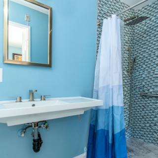 A modern bathroom with blue walls, featuring a sink, mirror, and tiled shower area.