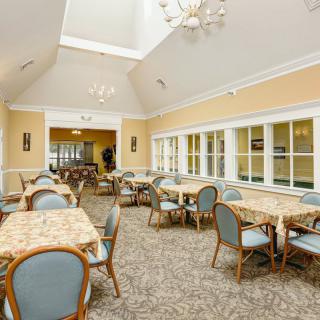 A well-lit dining room with multiple tables and chairs, set in a spacious interior.