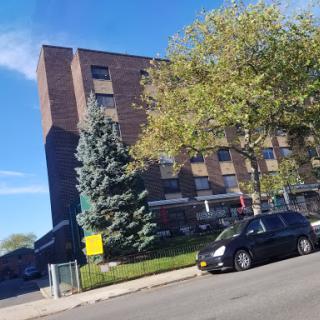 A view of a multi-story apartment building surrounded by trees and parked cars under a clear blue sky.