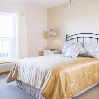 A bright and cozy bedroom with a neatly made bed, soft lighting, and ample natural light from the window.
