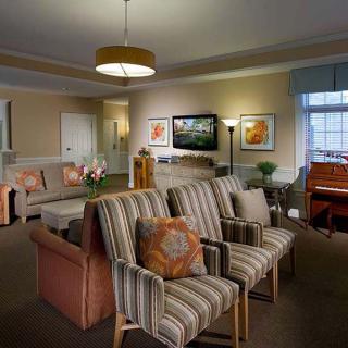 A cozy living room with striped chairs, a sofa, and a piano, creating a warm and inviting atmosphere.