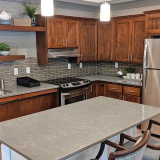 A modern kitchen with wooden cabinets and stainless steel appliances, featuring an island countertop and bar stools.