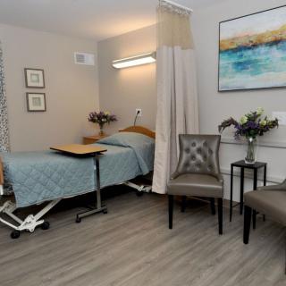 A well-furnished hospital room with a bed, chairs, and decorative elements.