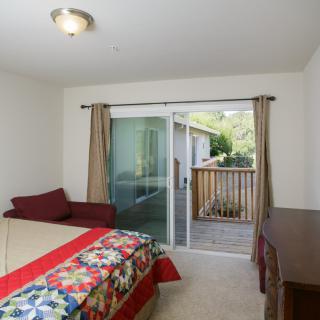 A cozy bedroom with a bed, sliding glass door leading to a balcony, and natural light streaming in.